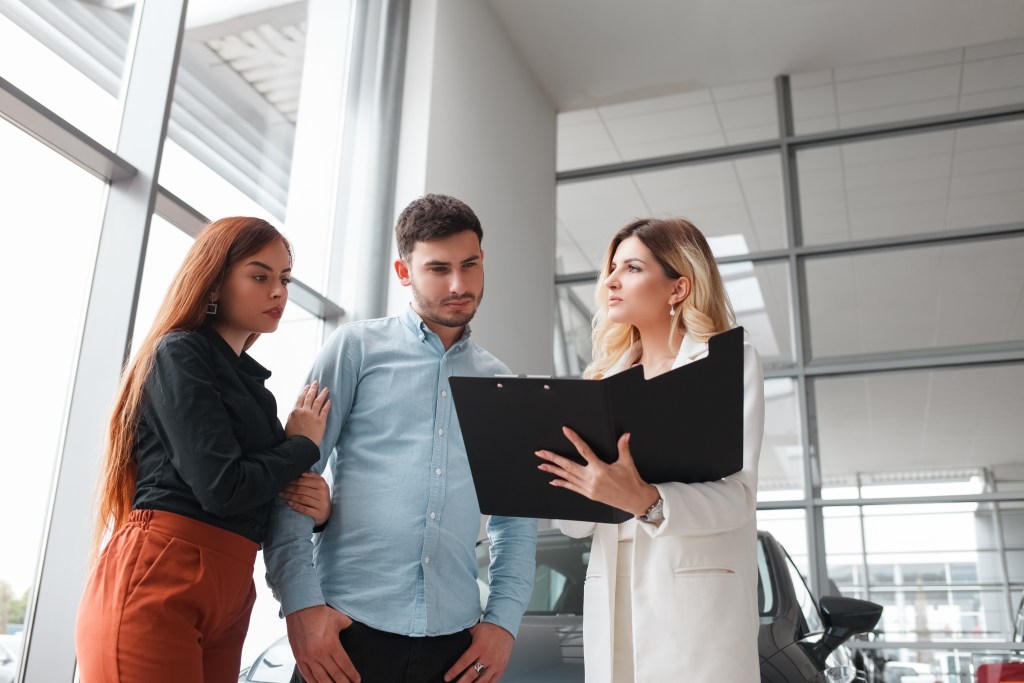 Female car saleswoman shows documents to a couple. Buying a car concept